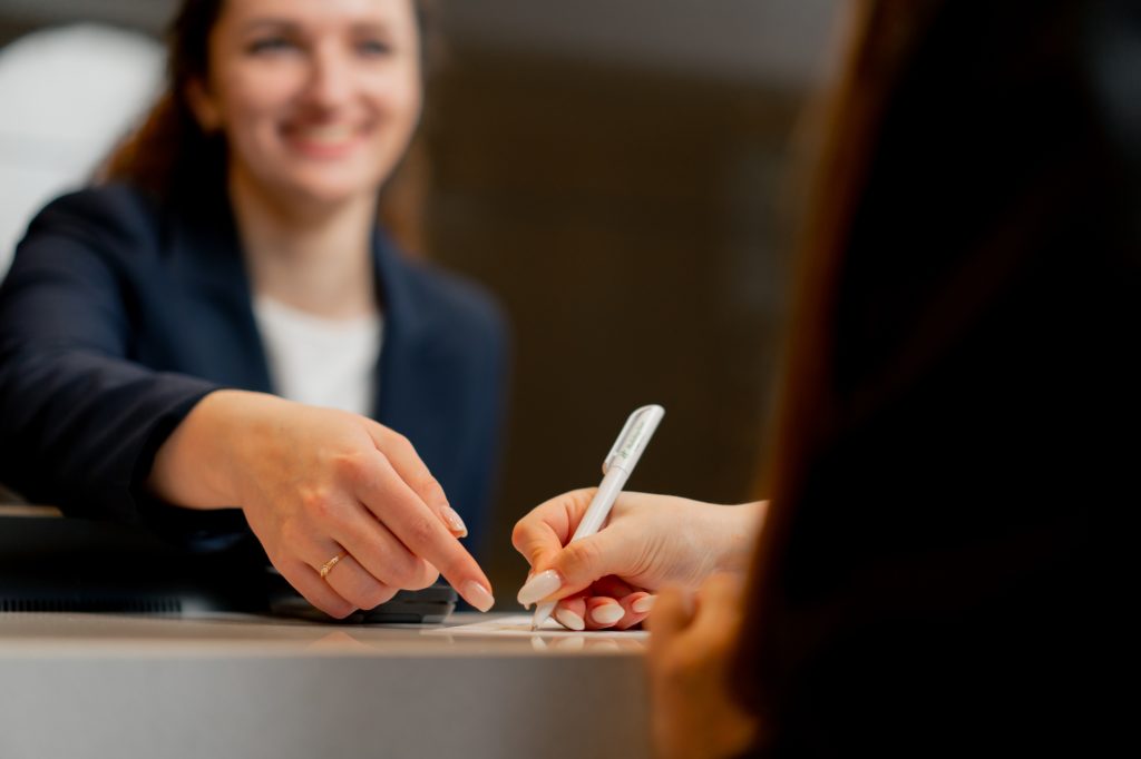 close-up of a smiling receptionist helping a guest to fill out registration form at the hotel