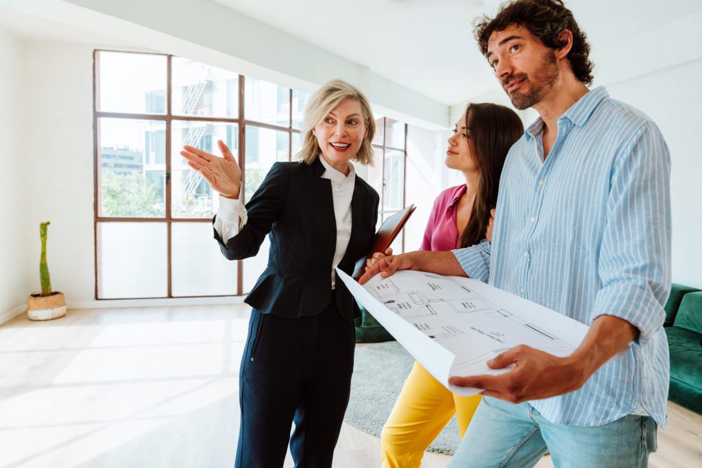 Real estate agent showing a new apartment and features of a good investment to a young couple. Woman and man buying a property in a rich area of the city.
