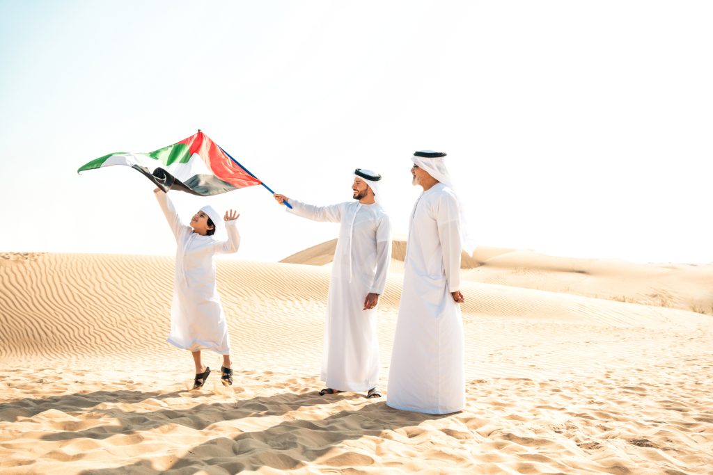 Three generation family making a safari in the desert of Dubai wearing white kandura outfit. Grandfather, son and grandson spending time together in the nature.