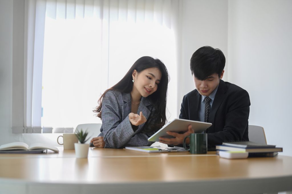 Two young businesspeople using digital tablet and discussing about business growth in modern office.