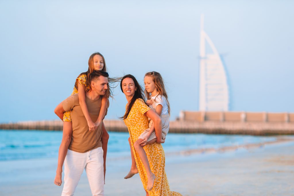 Happy family on the beach at summer vacation with Burj Al Arab on background in Dubai, UAE.