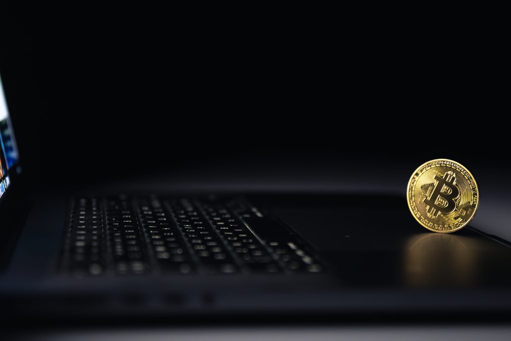 Bitcoin coin near laptop on black background. Finance and crypto money concept. High quality photo